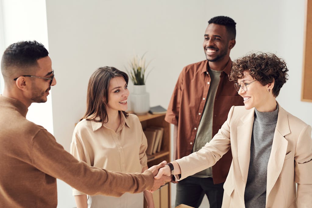 Four colleagues smiling and shaking hands in a bright office setting.